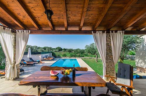 massiver Holztisch auf der großen schattigen Terrasse neben dem Swimmingpool, eine Villa für die Touristen, grünes Istrien, ein Bestimmungsort für den Urlaub  